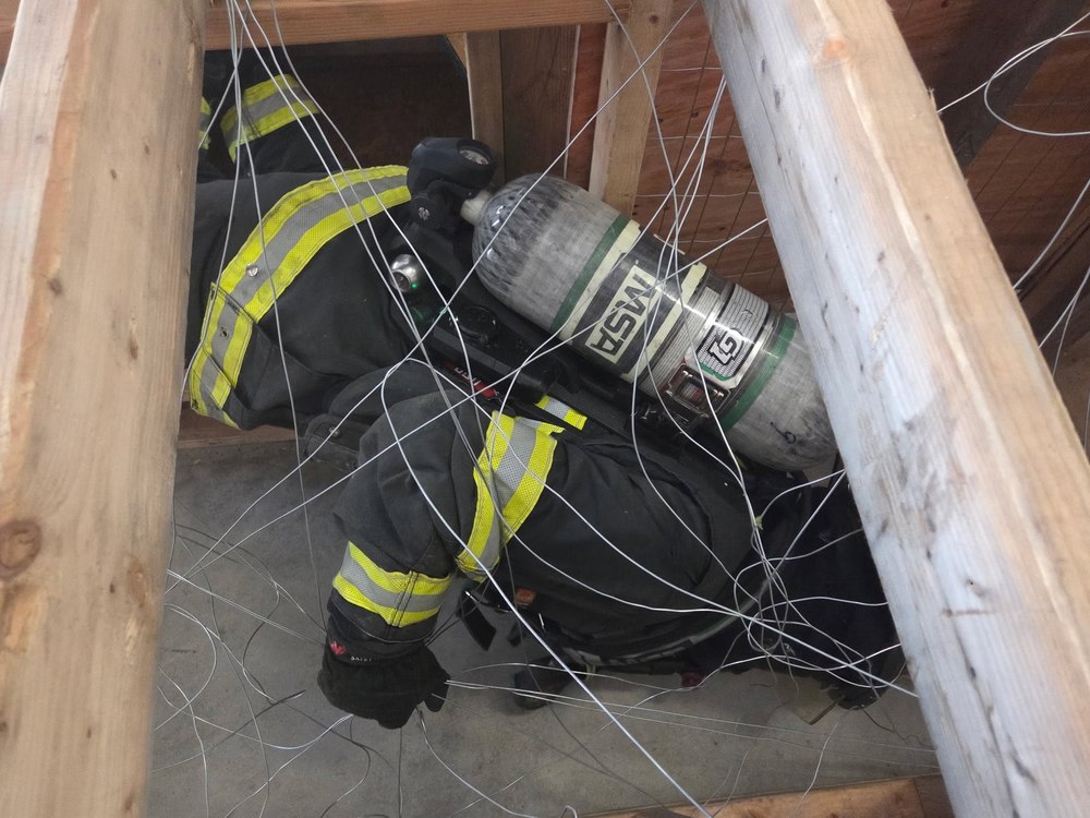 Firefighter navigating a confined-space wire maze training prop
