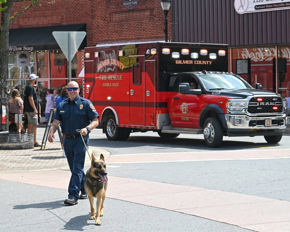 Gilmer County Fire/Rescue K9 handler walking through downtown Ellijay alongside a department ambulance