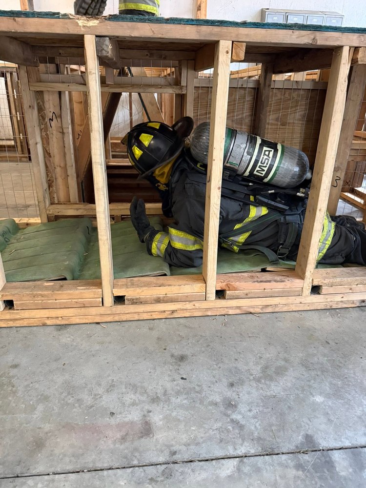 Firefighter in full gear crawling through a search-training maze prop