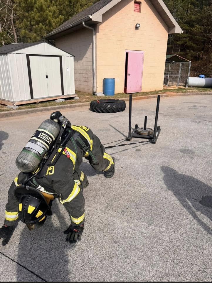 Probationary firefighter pushing a weighted sled in full turnout gear