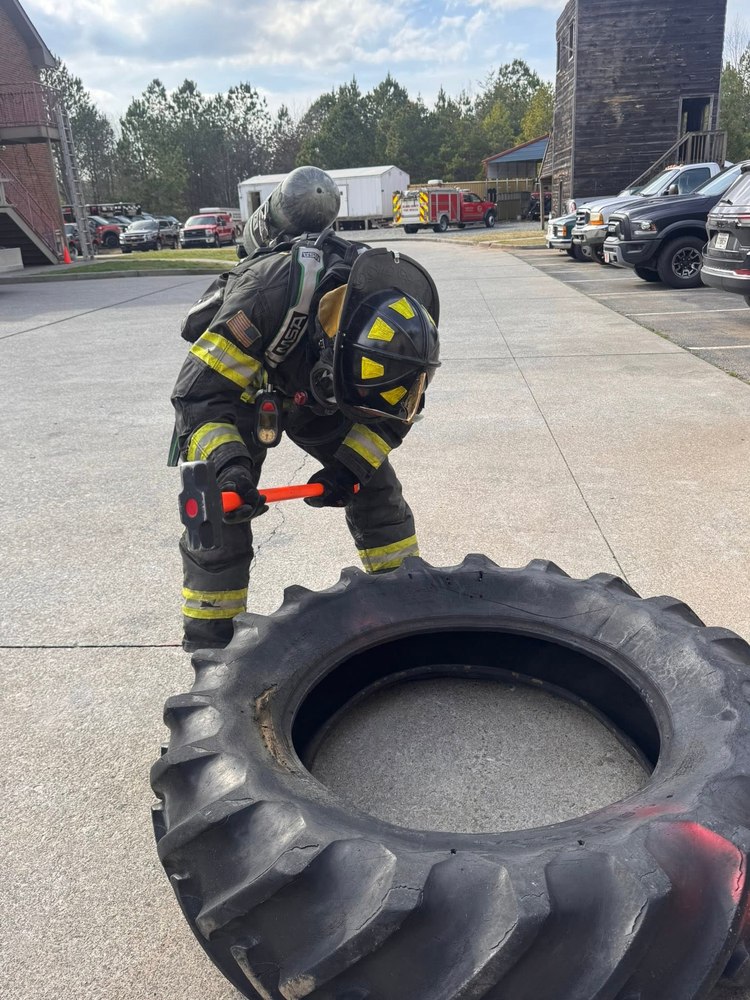 Firefighter in full turnout gear training with a sledgehammer on a tire prop